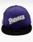 A 2-tone purple and black fitted hat with the San Diego Padres script logo, a 25th Anniversary side patch, and a pink under visor.
