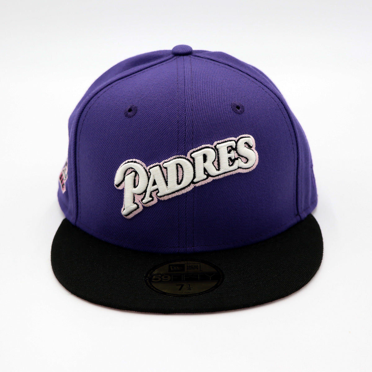 A 2-tone purple and black fitted hat with the San Diego Padres script logo, a 25th Anniversary side patch, and a pink under visor.